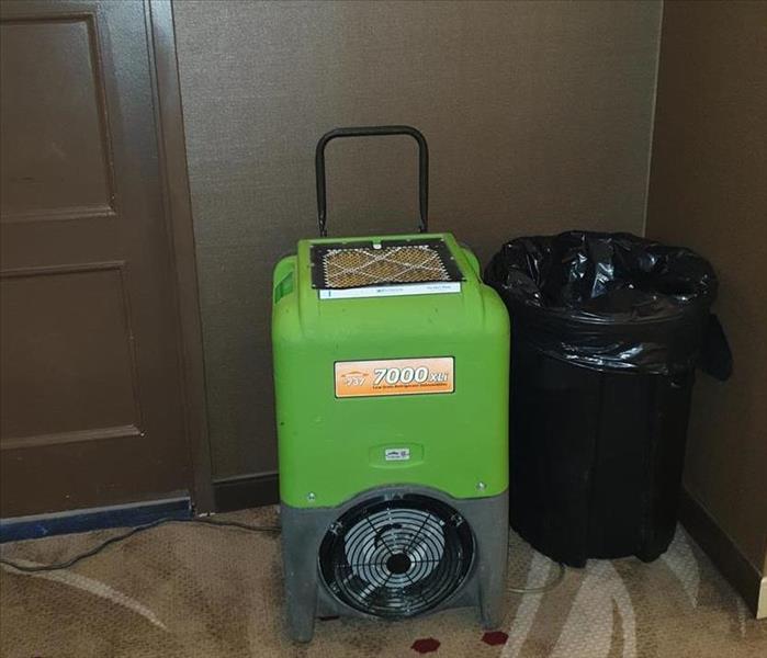Green Dehumidifier up against a brown paneled wall. 