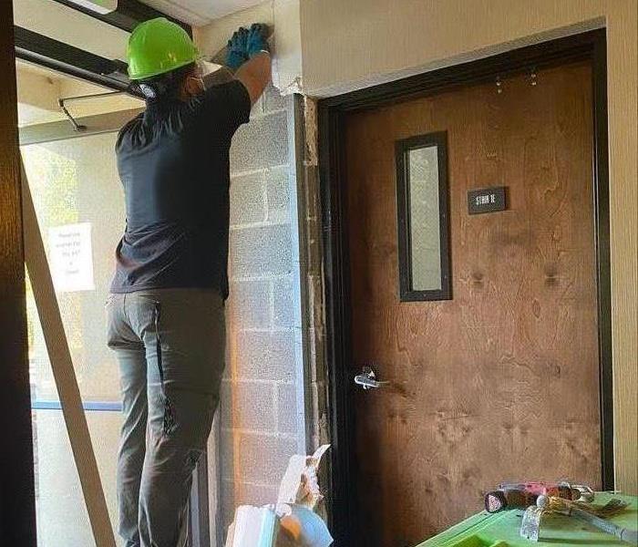 Man in green hard hat on a step ladder.