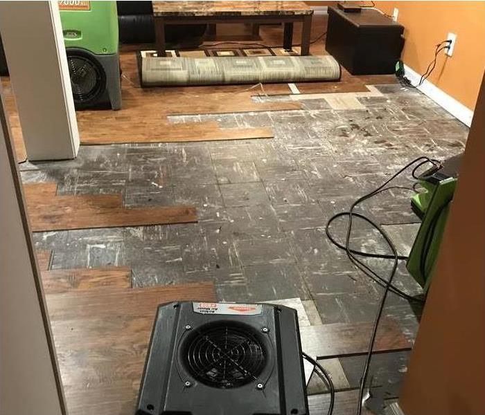 Wooden floor tiles removed due to water damage, air mover placed on damaged area